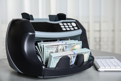 Modern electronic bill counter with money on table indoors