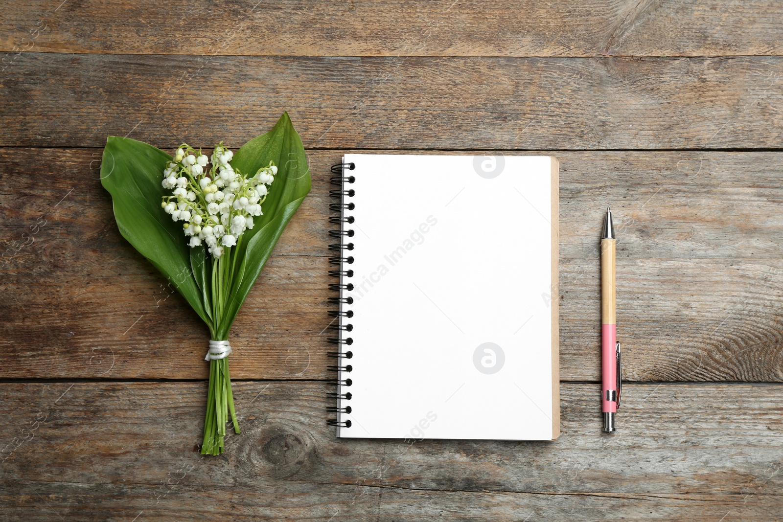 Photo of Notebook, pen and lily of the valley bouquet on wooden background, flat lay. Space for text
