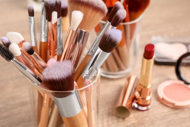 Photo of Set of professional brushes and makeup products on wooden table, closeup