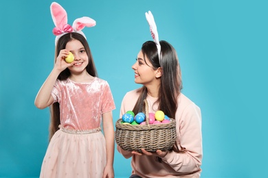 Photo of Mother and daughter in bunny ears headbands with basket of Easter eggs on color background
