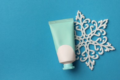 Tube of hand cream and snowflake on light blue background, flat lay with space for text. Winter skin care