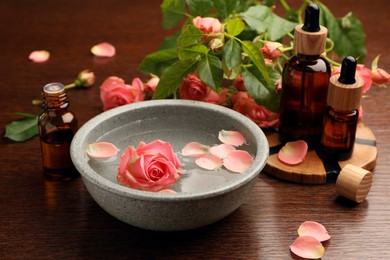Photo of Bowlwater, bottles with essential oil and beautiful rose petals on wooden table. Aromatherapy treatment