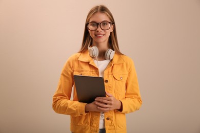 Teenage student with tablet and headphones on beige background