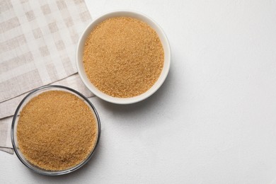 Photo of Brown sugar in bowls on white table, flat lay. Space for text