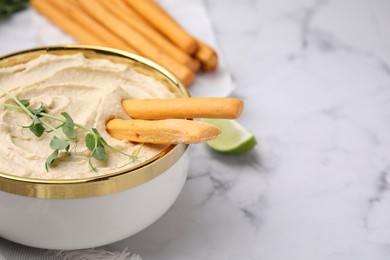 Delicious hummus with grissini sticks served on white marble table, closeup. Space for text