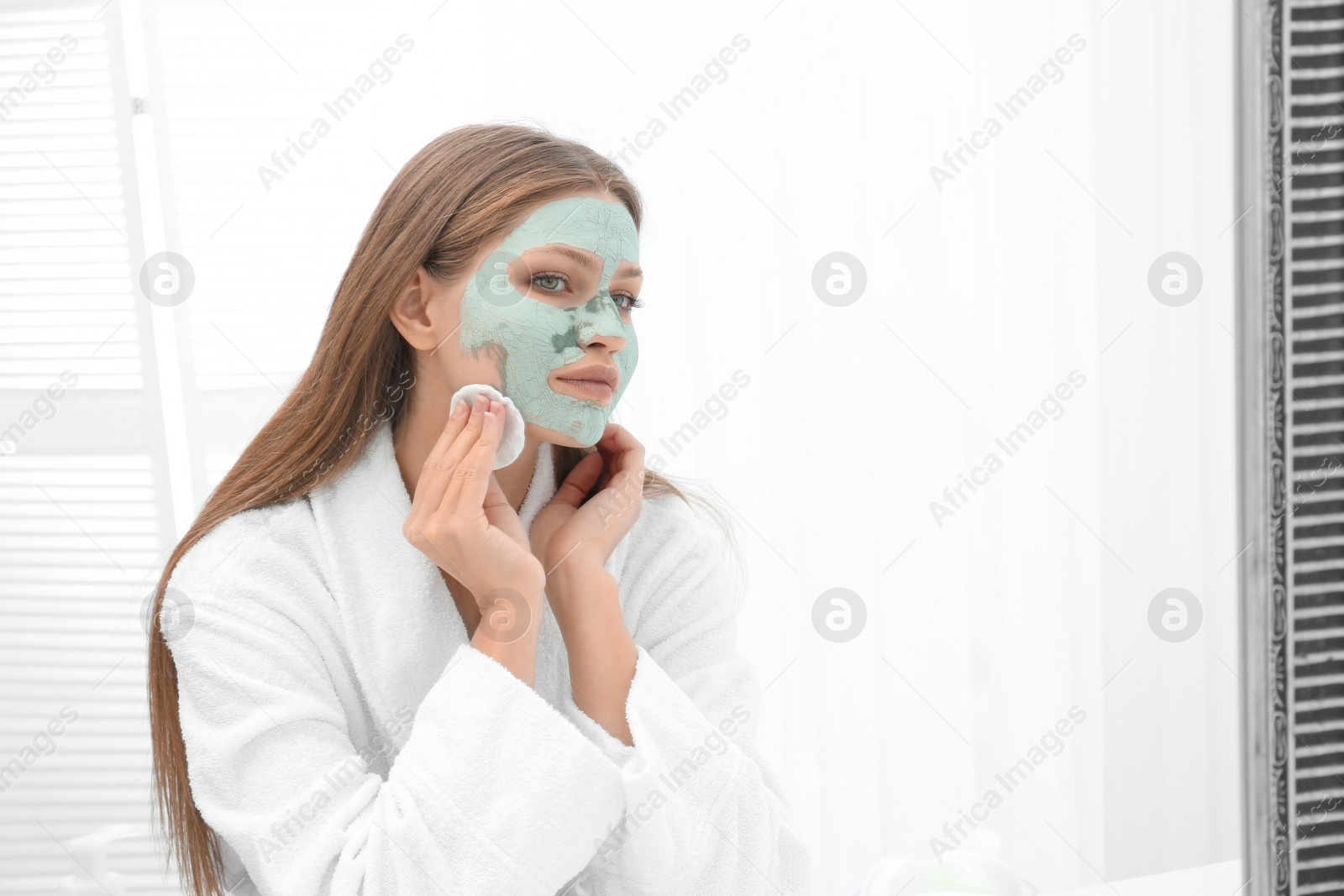 Photo of Beautiful woman removing homemade clay mask from her face indoors