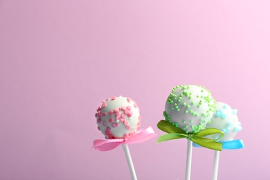 Photo of Tasty cake pops with bows on lilac background. Space for text