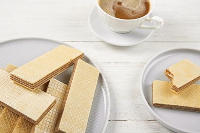 Plates of delicious wafers with cup of coffee  on white wooden background