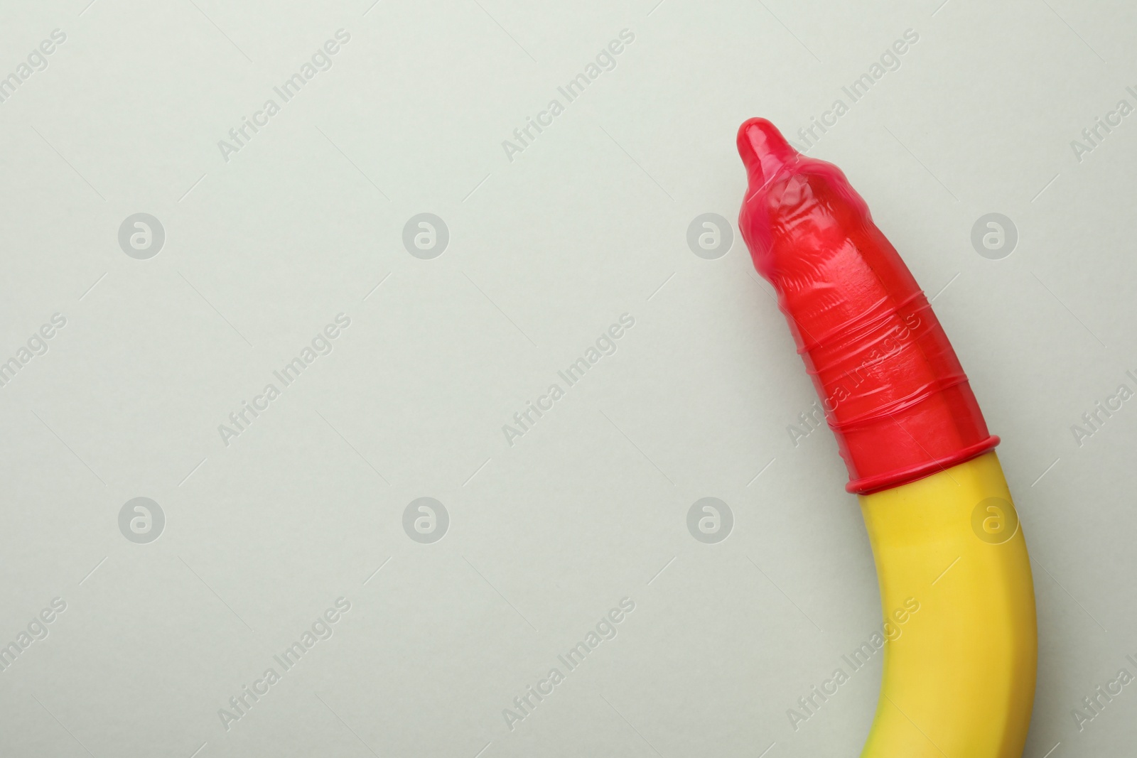 Photo of Banana with condom on light grey background, top view and space for text. Safe sex