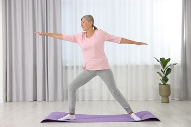 Senior woman practicing yoga on mat at home