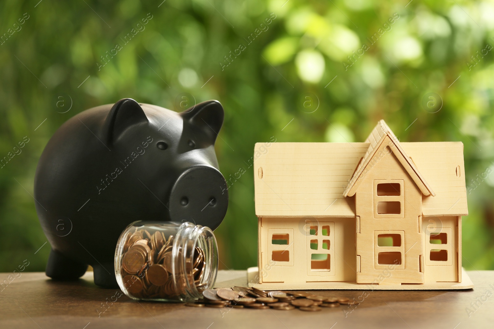 Photo of Piggy bank, house model and coins in glass jar on wooden table outdoors. Saving money concept