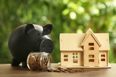 Piggy bank, house model and coins in glass jar on wooden table outdoors. Saving money concept