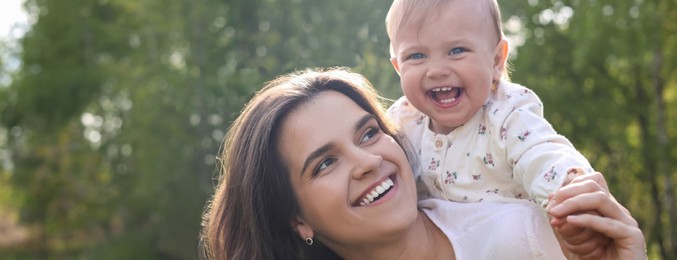 Image of Happy mother playing with her cute baby in park on sunny day, space for text. Banner design