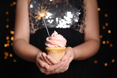 Woman holding birthday cupcake with sparkler on blurred background, closeup
