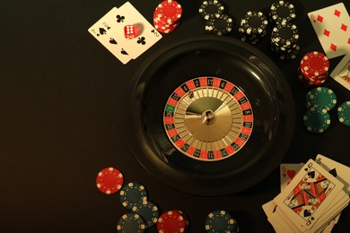 Photo of Roulette wheel, playing cards and chips on table, flat lay with space for text. Casino game