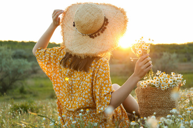 Photo of Woman with straw hat and handbag full of chamomiles resting in meadow