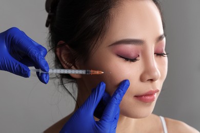 Woman getting facial injection on grey background, closeup