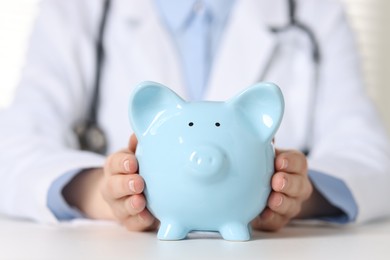 Photo of Doctor with piggy bank at white table, closeup