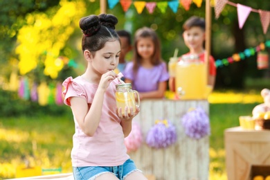 Cute little girl drinking natural lemonade in park, space for text. Summer refreshing beverage