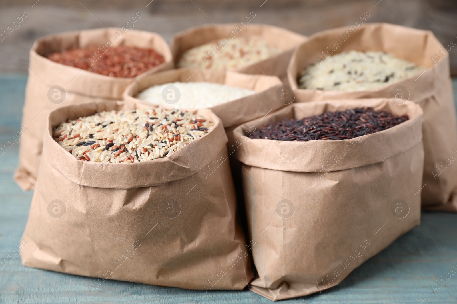 Photo of Brown and polished rice in paper bags on blue wooden table