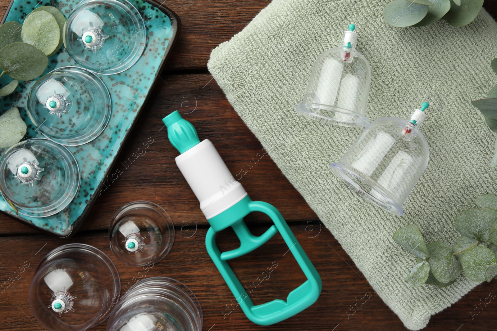 Photo of Cupping therapy. Plastic cups, hand pump, towel and eucalyptus leaves on wooden table, flat lay