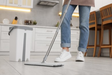 Woman cleaning floor with mop in kitchen, closeup