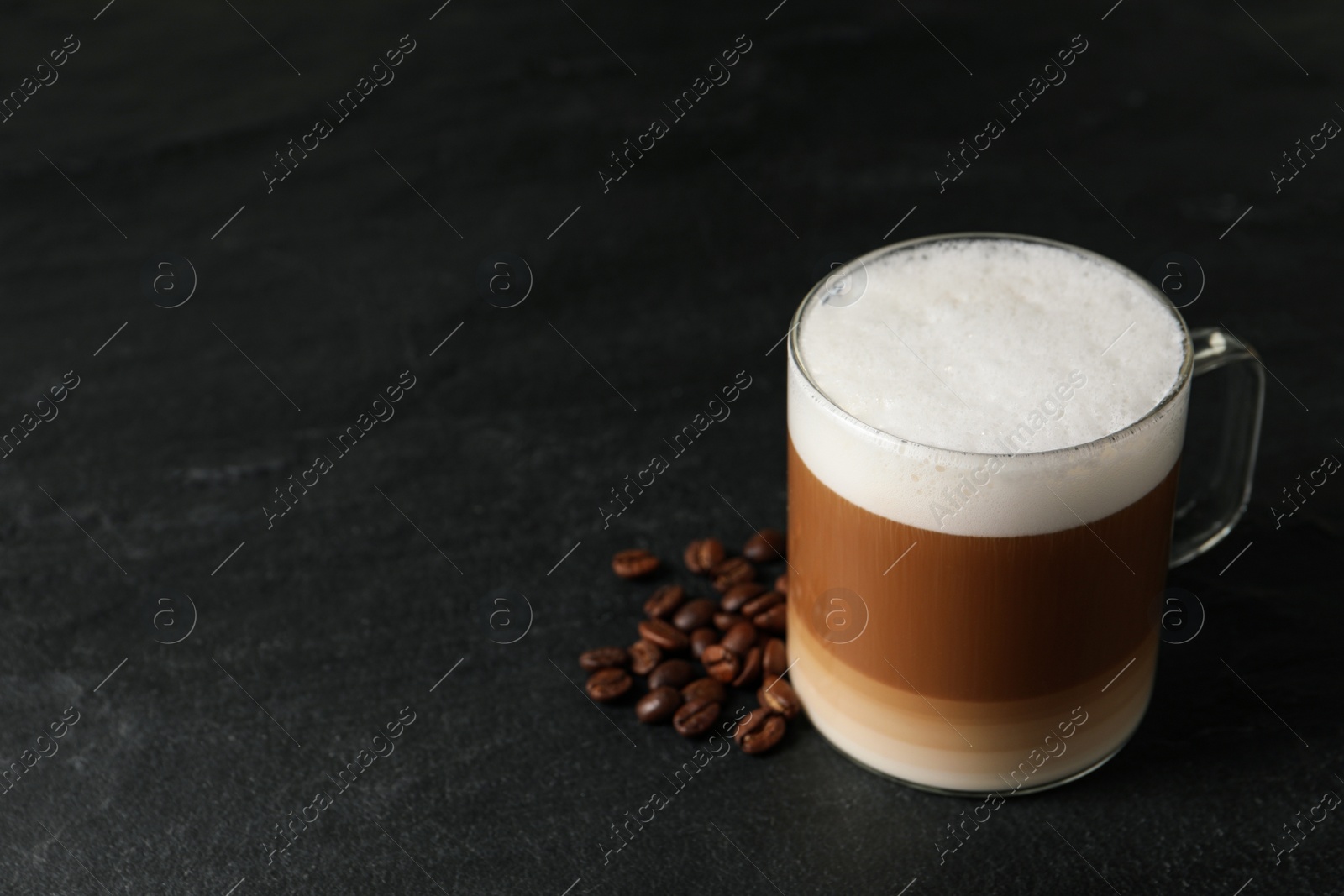 Photo of Glass cup of delicious layered coffee and beans on black table, space for text