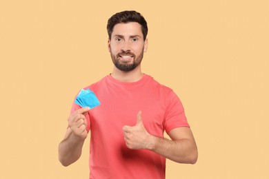 Photo of Happy man with condoms showing thumb up on beige background. Safe sex