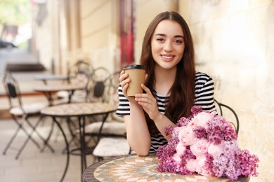 Beautiful woman with bouquet of spring flowers and coffee in outdoor cafe, space for text