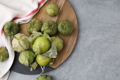 Photo of Fresh green tomatillos with husk on gray table, flat lay. Space for text