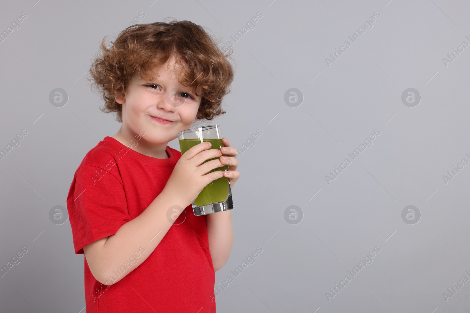 Photo of Cute little boy with glass of fresh juice on light gray background, space for text