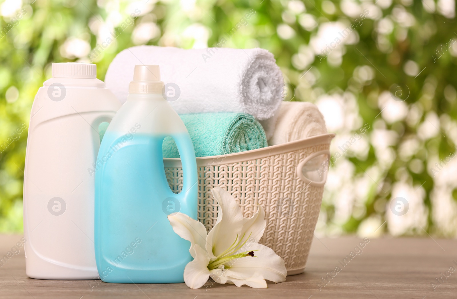 Photo of Clean towels in basket with lily and detergents on table against blurred background. Space for text