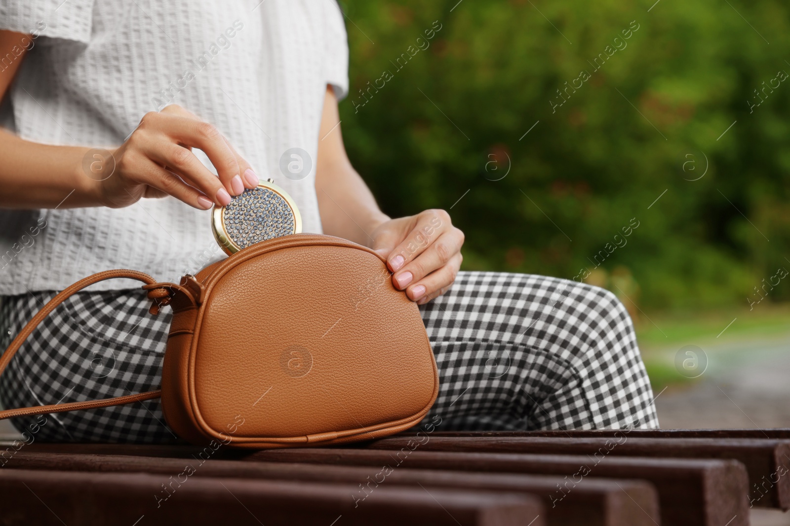 Photo of Woman taking cosmetic pocket mirror from bag on bench outdoors, closeup