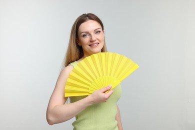 Happy woman with yellow hand fan on light grey background