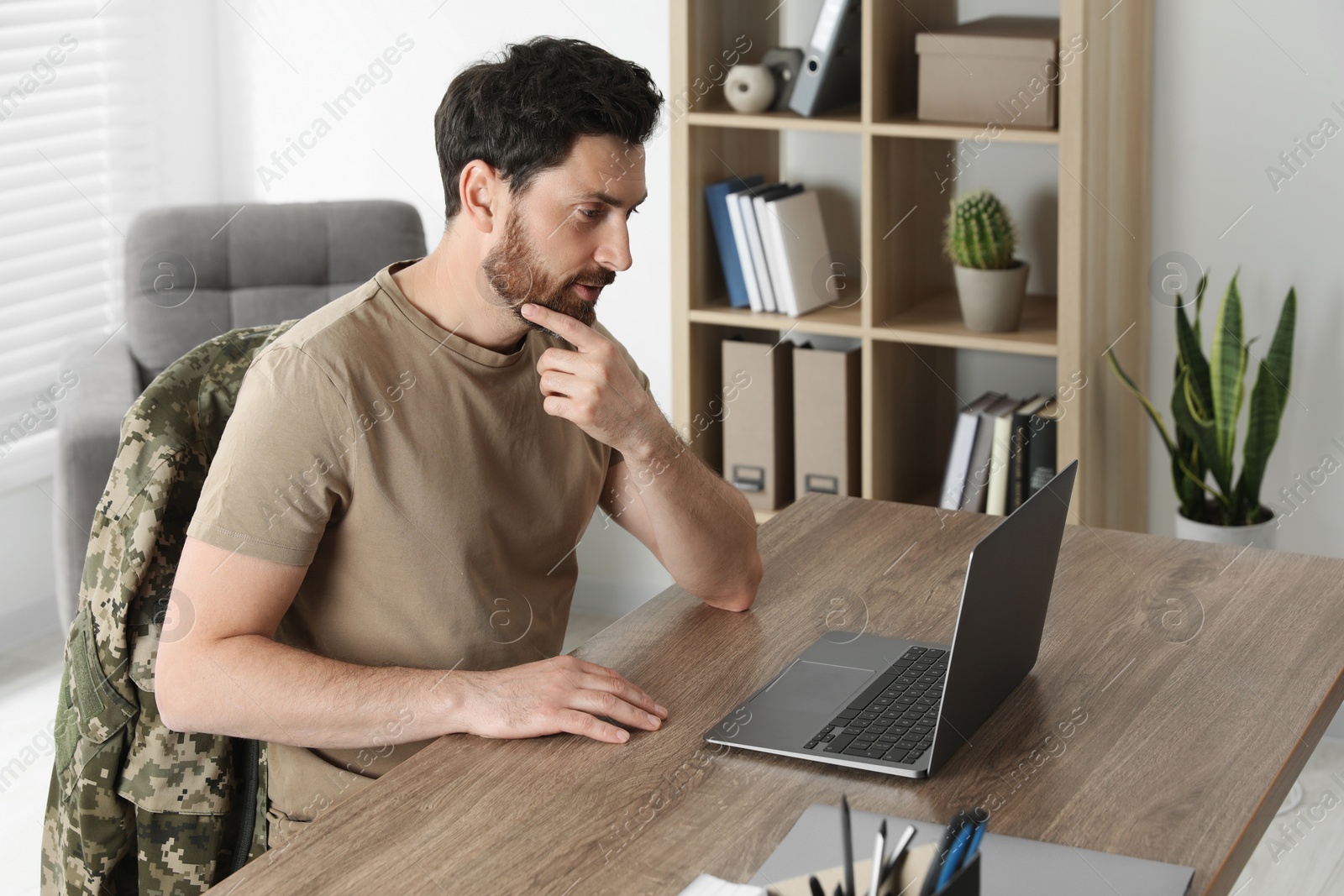 Photo of Soldier using laptop at wooden table indoors. Military service