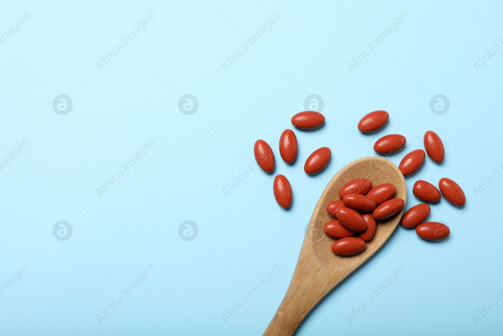 Photo of Wooden spoon with pills on light blue background, flat lay. Space for text