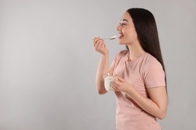 Photo of Happy woman eating tasty yogurt on grey background. Space for text