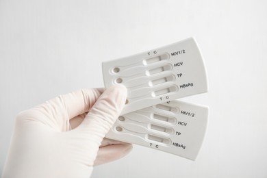 Photo of Doctor in gloves holding disposable express tests for hepatitis on white background, closeup