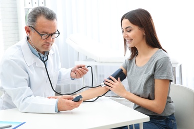 Young woman visiting doctor in hospital. Measuring blood pressure and checking pulse