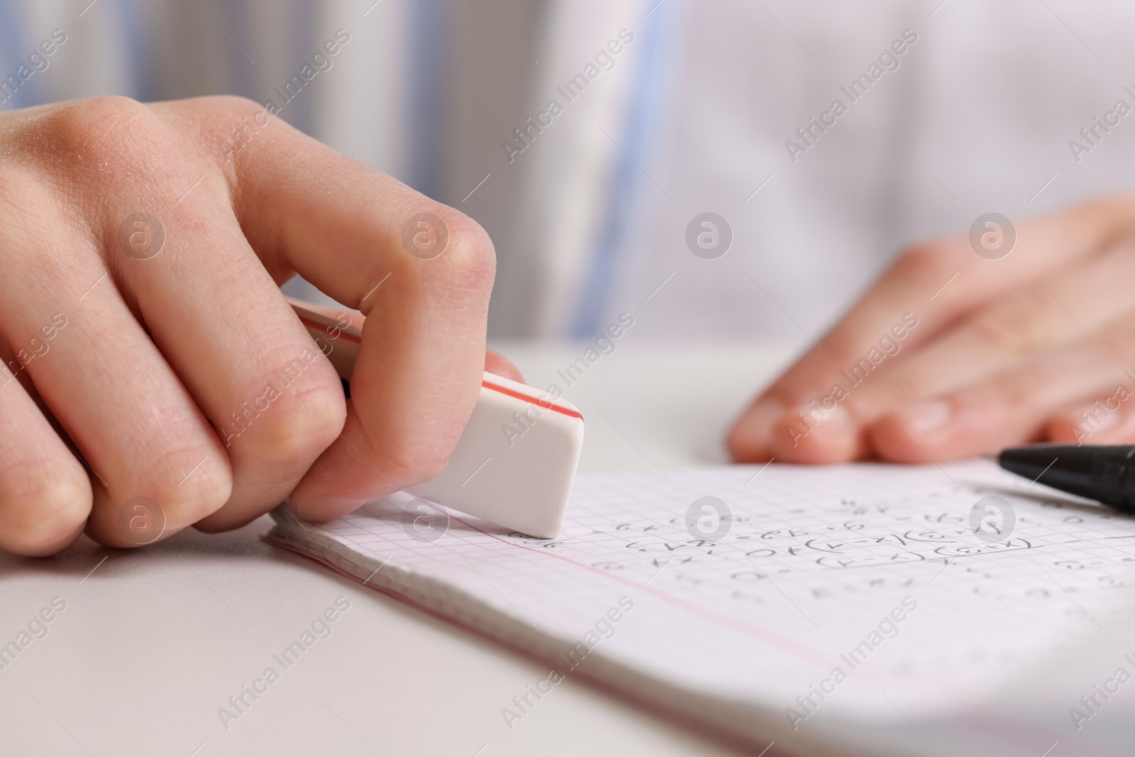 Photo of Girl erasing mistake in her notebook at white desk, closeup