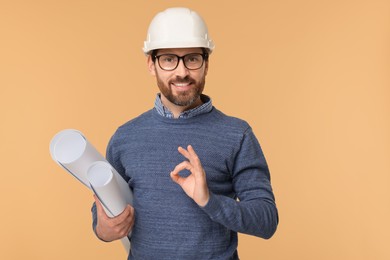 Architect in hard hat with drafts showing OK gesture on beige background