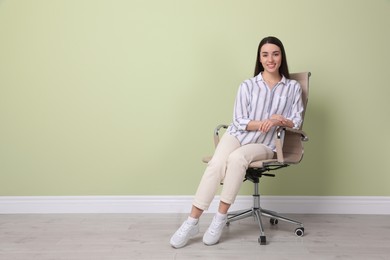 Photo of Young woman sitting in office chair near green wall indoors, space for text