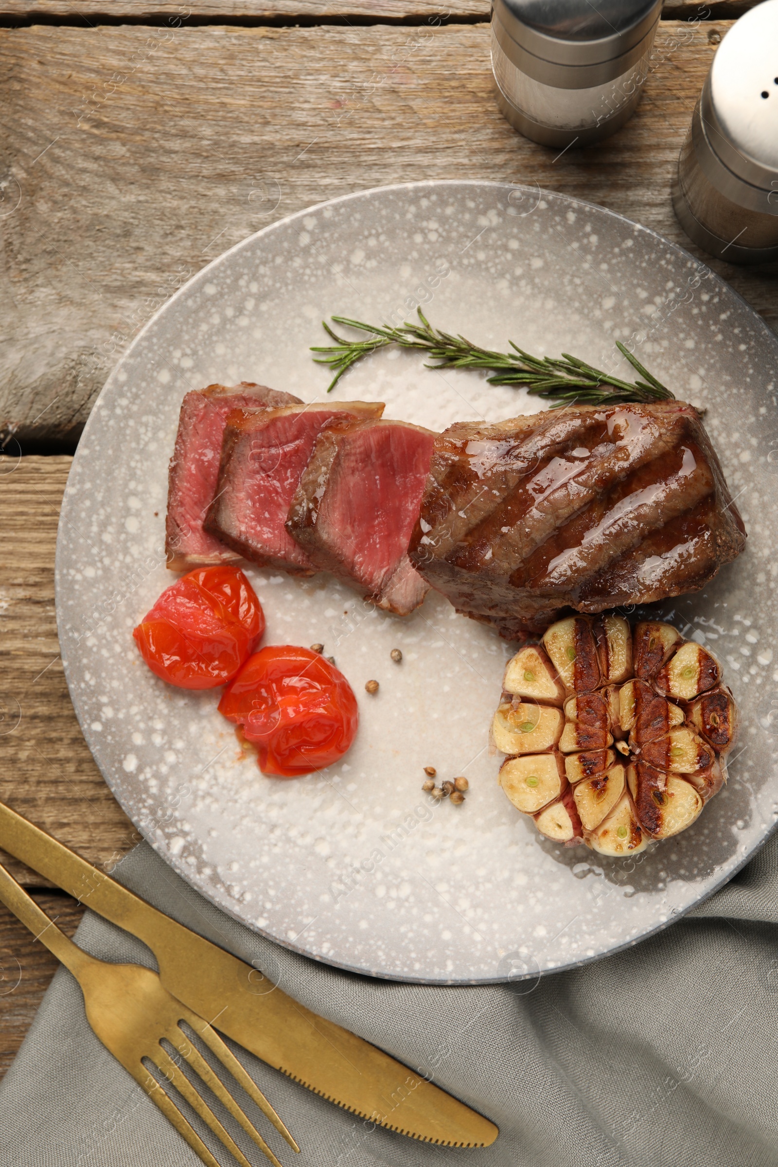 Photo of Delicious grilled beef steak served with spices and tomatoes on wooden table, top view