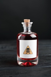 Photo of Glass bottle of poison with warning sign on black wooden table