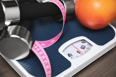 Photo of Scales, measuring tape, grapefruit and dumbbells on wooden table, closeup