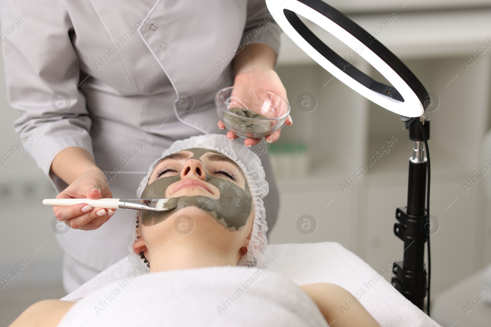 Photo of Cosmetologist applying mask on woman's face in clinic, closeup