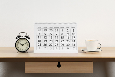 Photo of Calendar, alarm clock and cup of coffee on wooden table