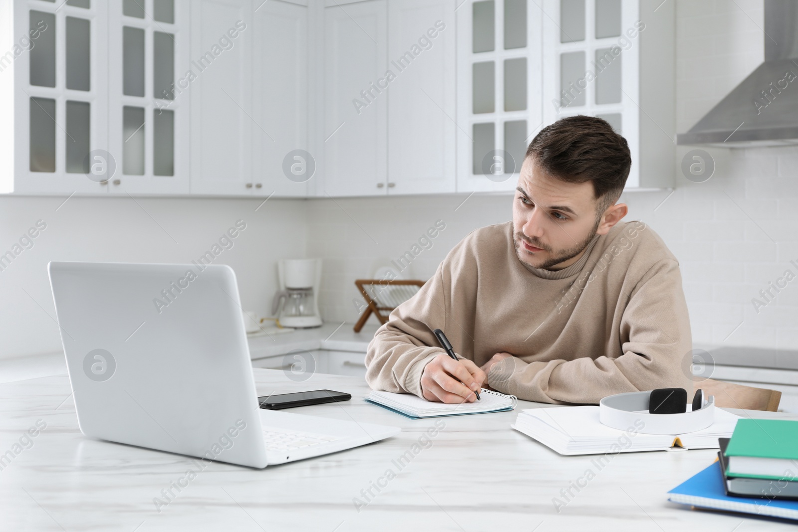 Photo of Young man using modern laptop for studying in kitchen. Distance learning