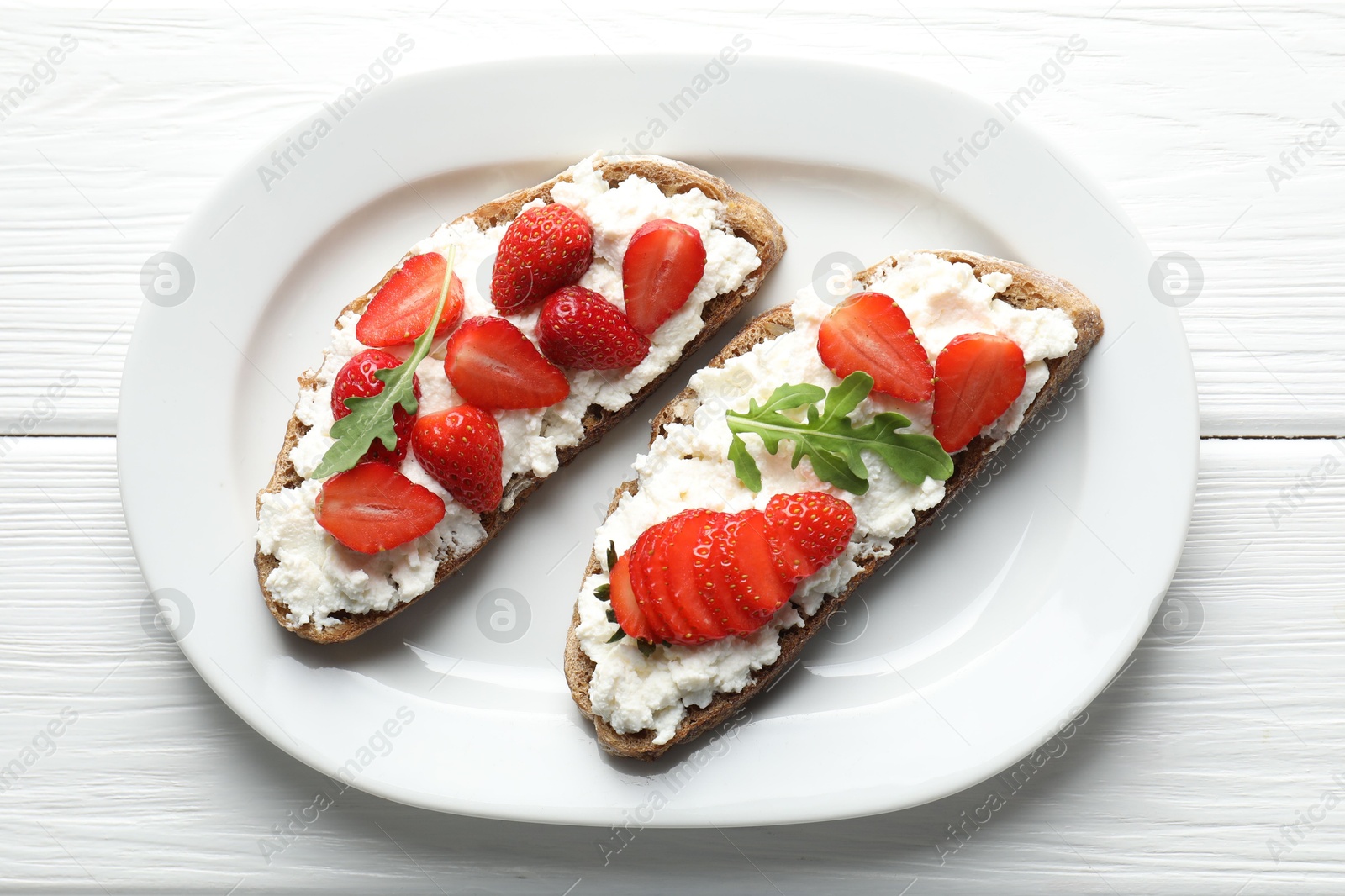 Photo of Delicious ricotta bruschettas with strawberry and arugula on white wooden table, top view