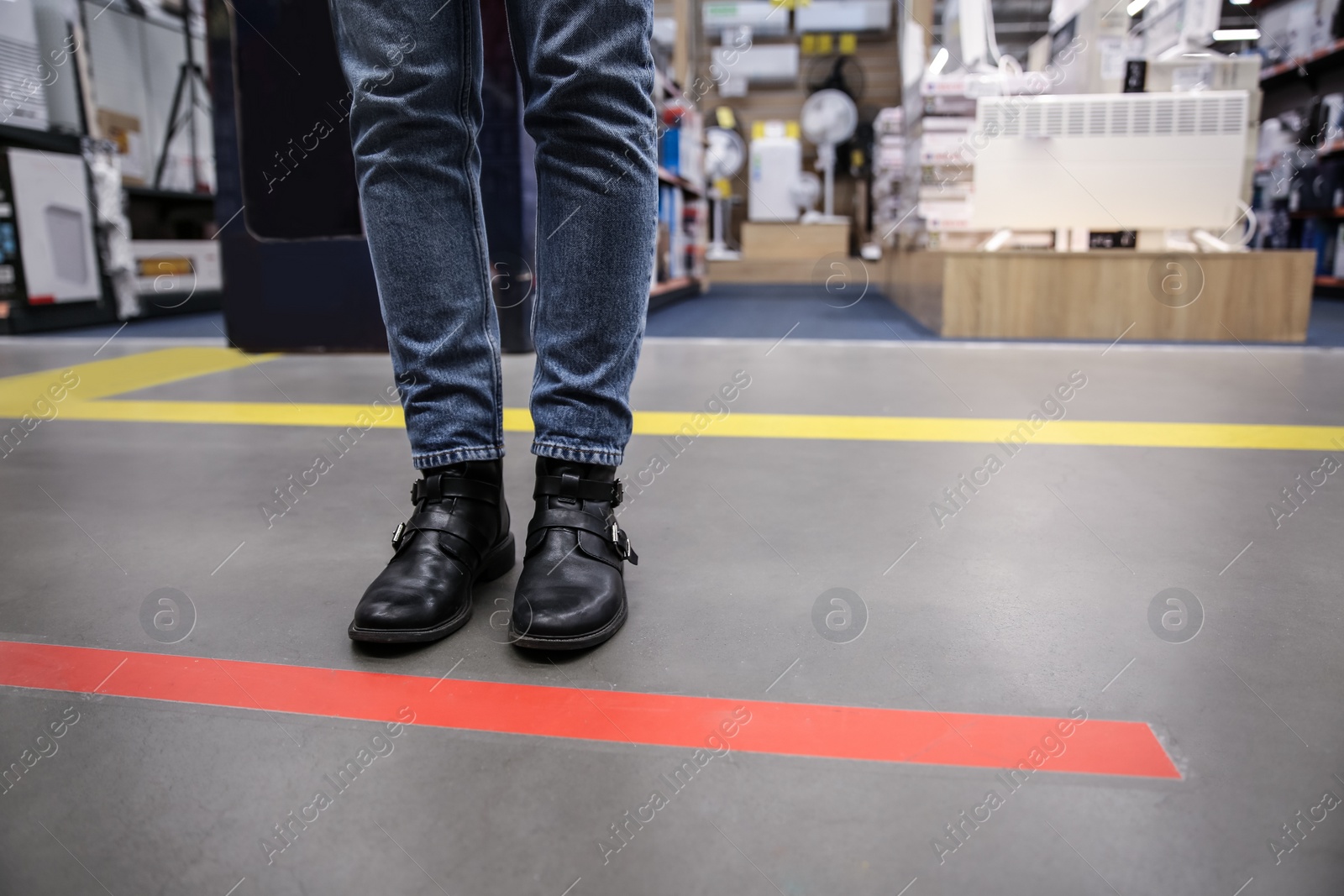 Photo of Person standing behind taped floor marking indoors for social distance, closeup. Preventive measure during coronavirus pandemic